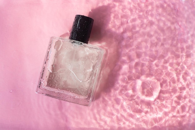 Frasco de perfume no fundo e gotas de água um frasco de perfume sem inscrições cheirar perfume em um fundo rosa gotas de água copiar espaço