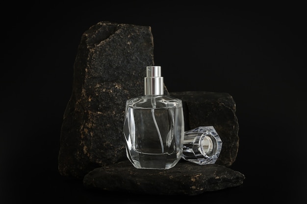 Frasco de perfume sem marca em pé no pódio de pedra. Apresentação do perfume no fundo preto. Brincar. Conceito de tendência em materiais naturais. Essência feminina e masculina. Cosmético natural.