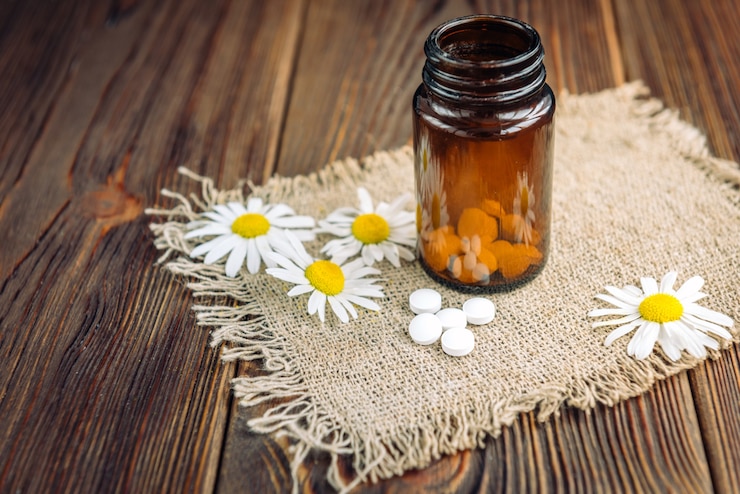 Foto frasco de pílulas de ervas brancas e flores de camomila em madeira escura, medicamento homeopático.