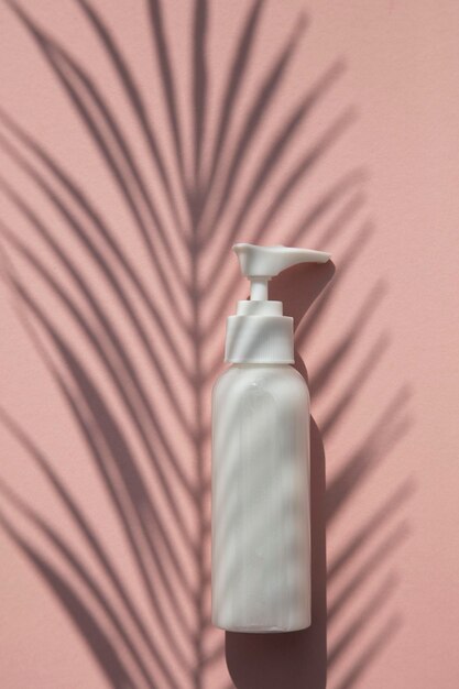 Frasco de produto cosmético branco com sombra de folha de palmeira tropical