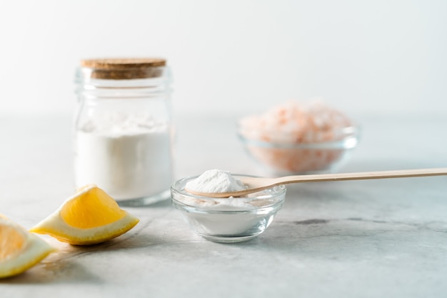 Frasco de produtos de limpeza naturais ecológicos com bicarbonato de sódio, sal rosa de limão e colher de pau na mesa de mármore