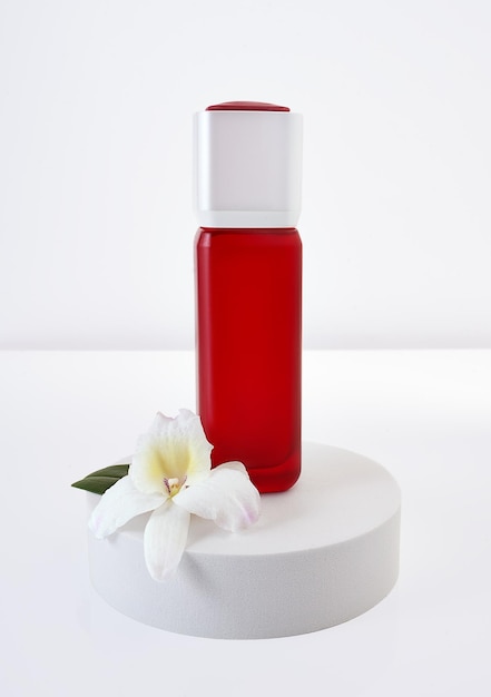 Frasco de recipiente cosmético de vidro vermelho com flor de orquídea no pódio branco