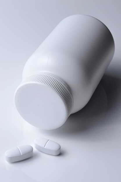 Frasco de remédio de plástico branco e fundo claro de duas pílulas brancas