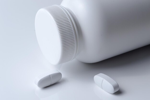 Frasco de remédio de plástico branco e fundo claro de duas pílulas brancas