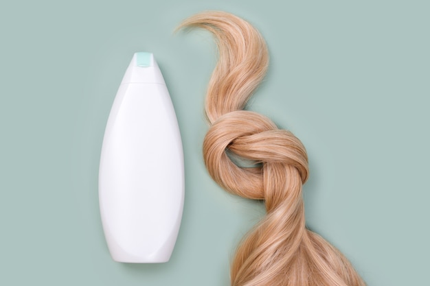 Frasco de shampoo ou condicionador e mecha de cabelo loiro com um nó. Fio de cabelo loiro cor de mel, vista superior. Serviço de cabeleireiro, força do cabelo, corte de cabelo, penteado, extensão de cabelo, conceito de tratamento.