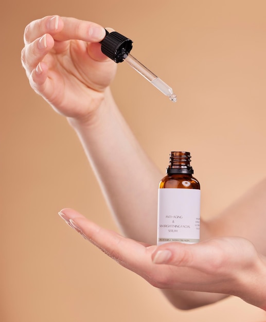 Frasco de soro de mãos e pipeta para cuidados com a pele em estúdio isolado em um fundo marrom Cosméticos de produtos dermatológicos e mulher ou modelo com retinol de ácido hialurônico ou óleo essencial para antienvelhecimento