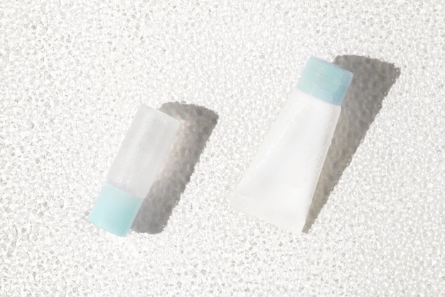 Frasco de soro modelo branco e tubo de creme em luz solar brilhante em superfície de vidro imitando a água