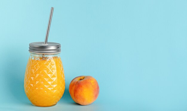 Frasco de suco de pêssego com canudo reutilizável de metal sobre fundo azul. Copie o espaço