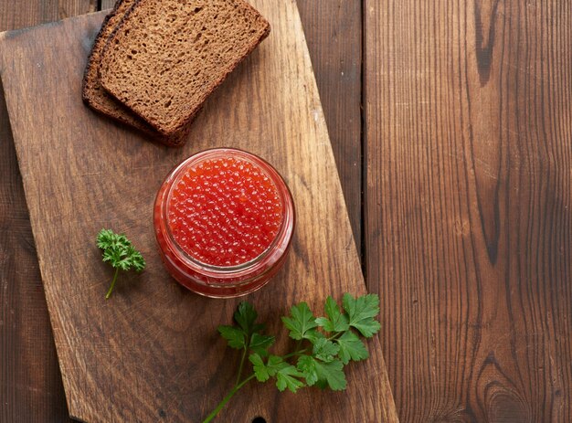 Frasco de vidro cheio com caviar vermelho em uma mesa de madeira marrom, vista superior