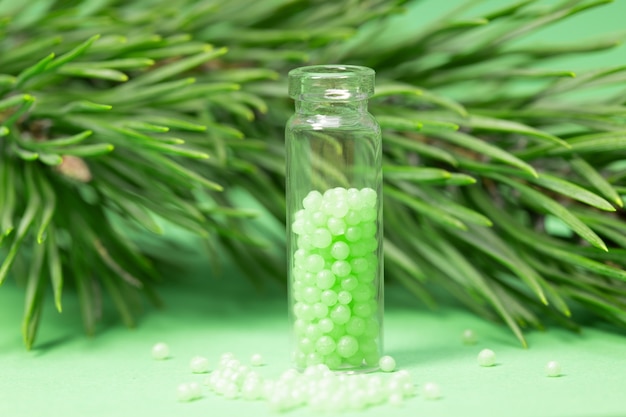 Frasco de vidro com grânulos verdes e um galho de pinheiro. remédios homeopáticos