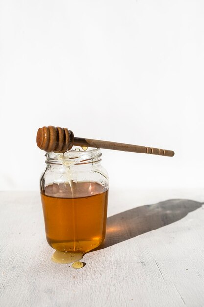 Frasco de vidro com mel cru de abelhas com gotas de mel e colher de mel