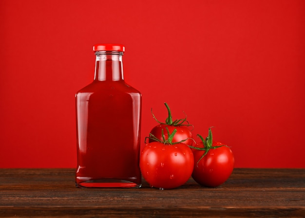 Frasco de vidro com molho de ketchup e tomates vermelhos frescos na mesa