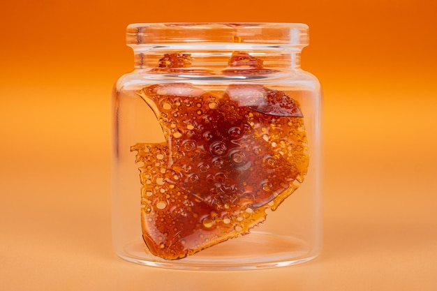 Frasco de vidro com pedaços de cera de cannabis marrom de resina endurecida de extrato de maconha em um fundo laranja