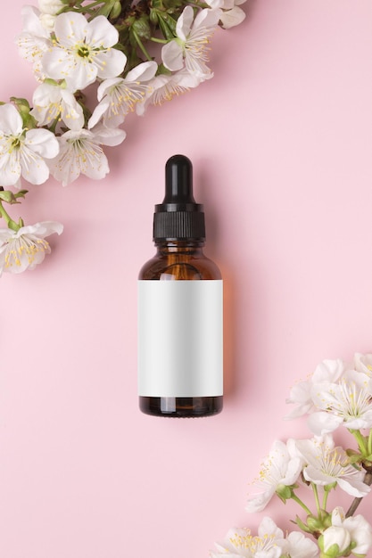 Frasco de vidro com soro de óleo em fundo rosa com cereja florescendo Minimalismo plano Ferramentas cosméticas