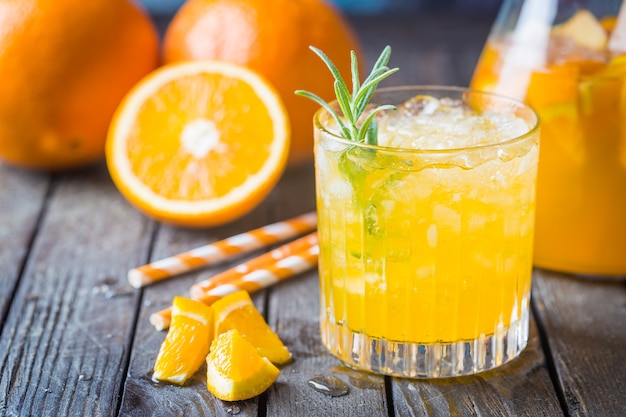 Frasco de vidro com suco de laranja fresco com gelo e frutas frescas na mesa escura