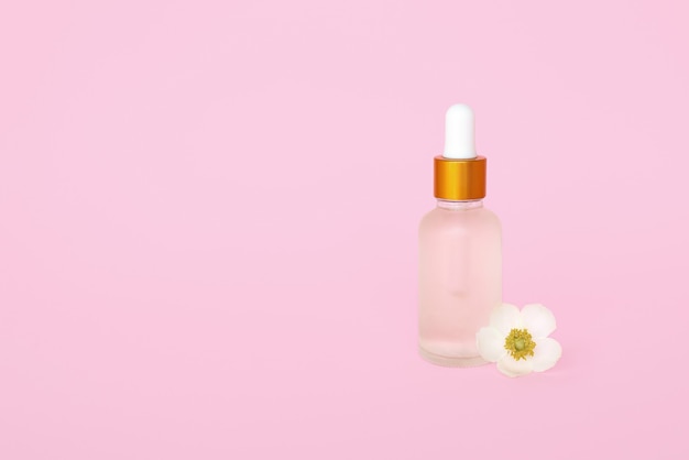 Frasco de vidro cosméticos com óleo. recipiente para um produto para mulheres com pequenas flores brancas sobre fundo turquesa. frasco cosmético. lugar para texto