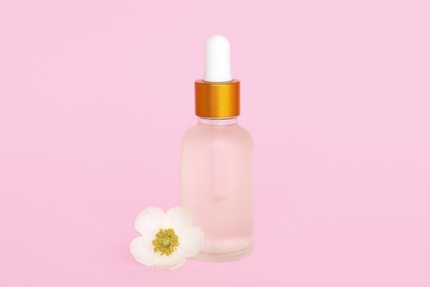 Frasco de vidro cosmetik com óleo. recipiente para um produto para mulheres com pequenas flores brancas sobre fundo turquesa. Frasco cosmético. Lugar para texto