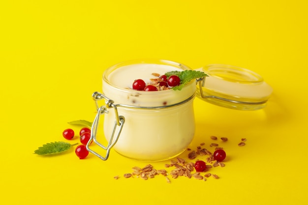 Frasco de vidro de iogurte de creme de leite com cranberry, hortelã e granola na superfície amarela