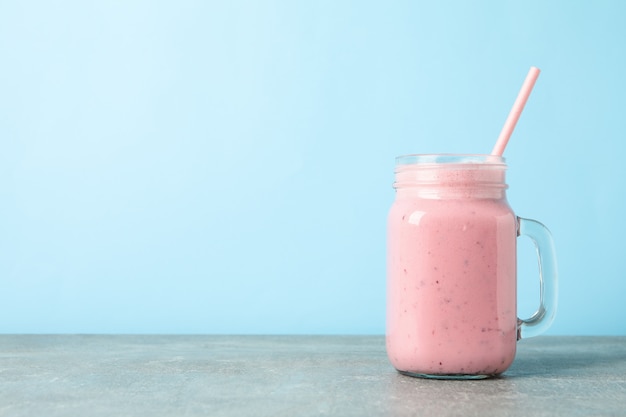 Frasco de vidro de milk-shake de morango na mesa cinza contra azul