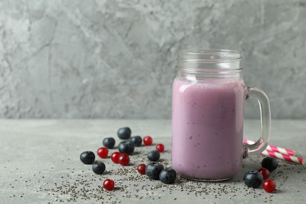 Frasco de vidro de smoothie, ingredientes e canudos na mesa texturizada cinza