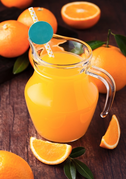 Frasco de vidro de suco de laranja orgânico fresco com laranjas cruas no fundo escuro de madeira