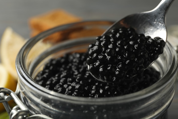 Frasco de vidro e colher com caviar preto, close-up