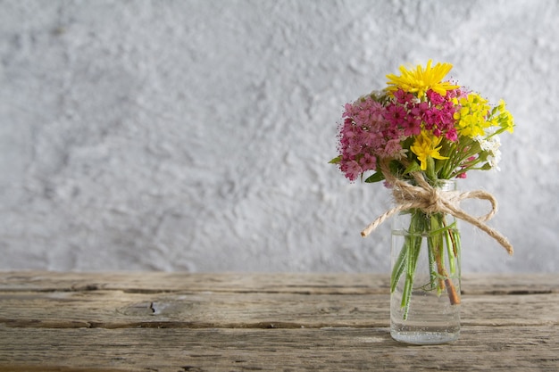 Frasco de vidro em miniatura com flores na mesa de madeira