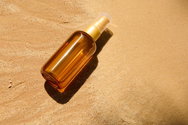 Frasco de vidro escuro sem marca com óleo spf ou loção corporal protetor solar no fundo da praia de areia conceito cosmético de verão