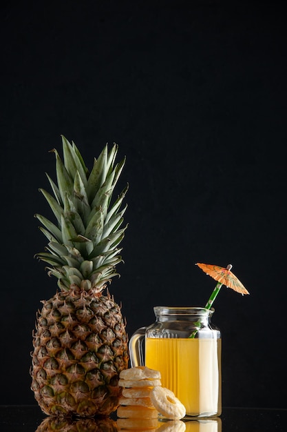 Frasco de vidro para coquetel com suco e guarda-chuva de coquetel de abacaxi seco anéis de abacaxi em fundo preto