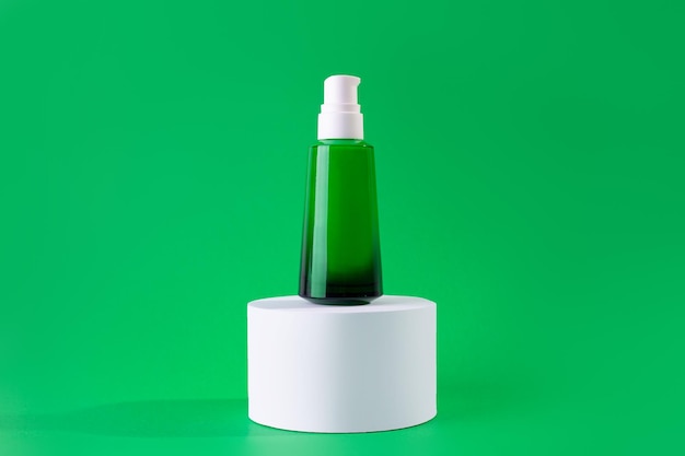 Frasco de vidro verde de creme ou soro em um pódio branco sobre fundo verde Modelo de Design