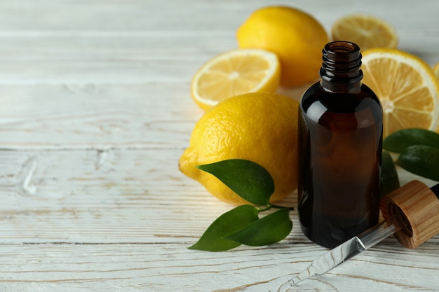 Frasco gotero con aceite y limones sobre mesa de madera blanca