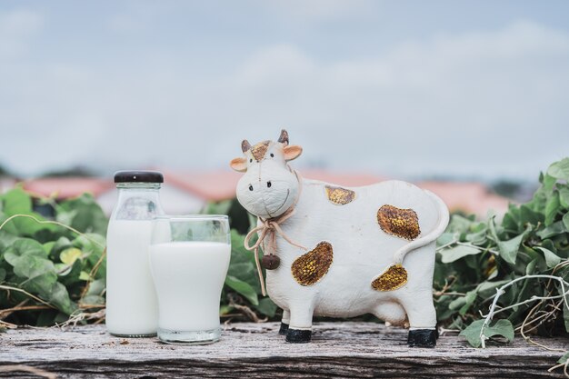 El frasco de leche con desenfoque de resina, leche, muñeca de vaca en la naturaleza y el fondo de cielo azul.