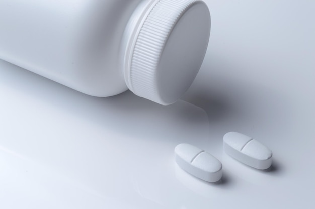 Frasco de medicina de plástico blanco y dos pastillas blancas de fondo claro