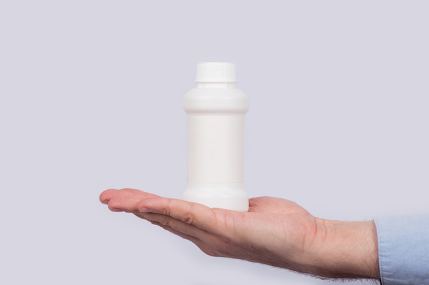 Frasco de medicina de plástico blanco en la palma de la mano de cerca.