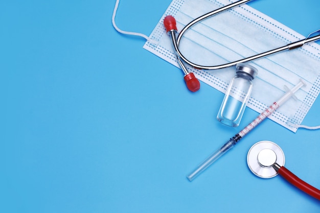 Frasco médico, frasco, seringa, estetoscópio e máscara facial em fundo azul com espaço de cópia. Vacinação
