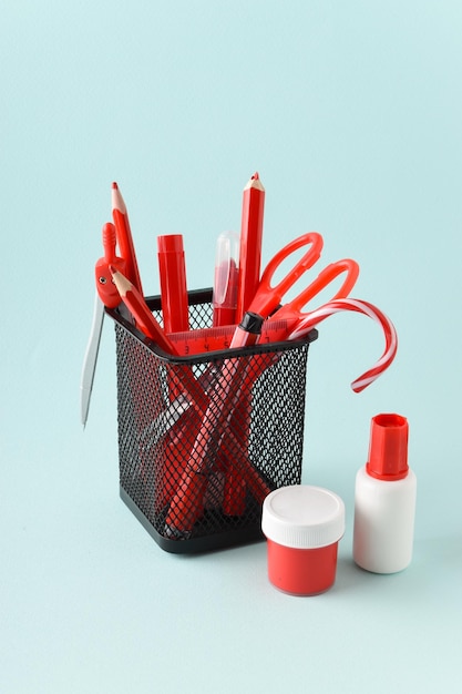 Frasco de metal negro con bolígrafos y lápices rojos sobre un fondo azul claro Espacio para útiles escolares para copiar