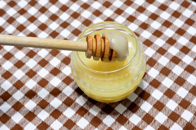 frasco con miel y cucharón de miel aislado en la vista superior de la toalla marrón a cuadros