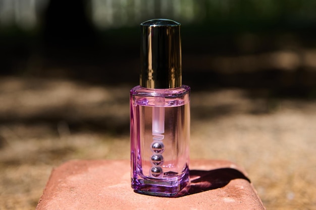 Frasco morado de vidrio transparente con producto cosmético para el cuidado de la piel debajo de los ojos sobre piedra rosa en el fondo de la naturaleza