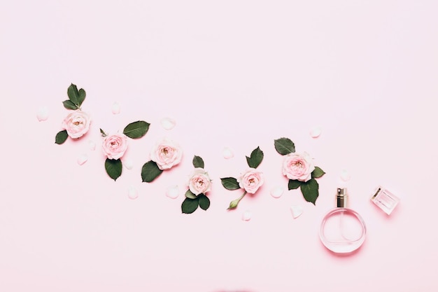 Frasco de perfume y arreglo floral de capullos de rosa sobre fondo rosa.