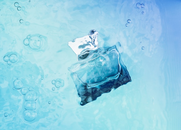Frasco de perfume azul transparente bajo el agua, ondas por encima de él.