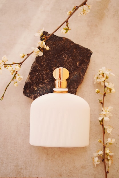 Foto frasco de perfume blanco sobre una piedra con ramas verdes sobre beige