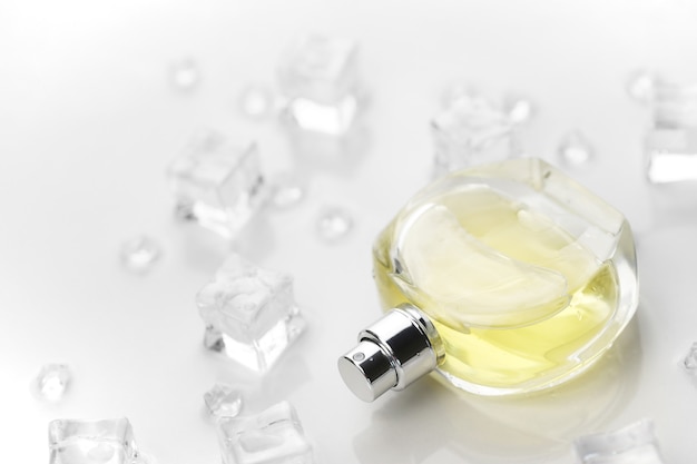 Frasco de perfume femenino amarillo, fotografía objetiva del frasco de perfume en cubitos de hielo y agua en el cuadro blanco