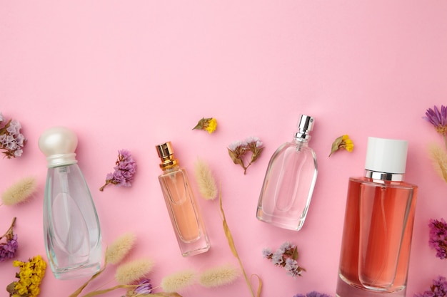 Frasco de perfume con flores en superficie rosa con espacio de copia