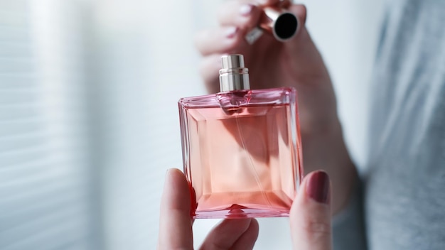 Frasco de perfume en una mano femenina contra el fondo del interior de la sala de luz