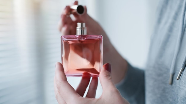 Frasco de perfume en una mano femenina sobre el fondo del interior de la habitación luminosa Eau de toilette eau de parfum concepto de belleza