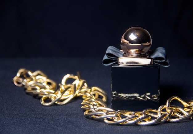 Un frasco de perfume de mujer negro sobre un fondo oscuro Decoración en forma de cadena de oro