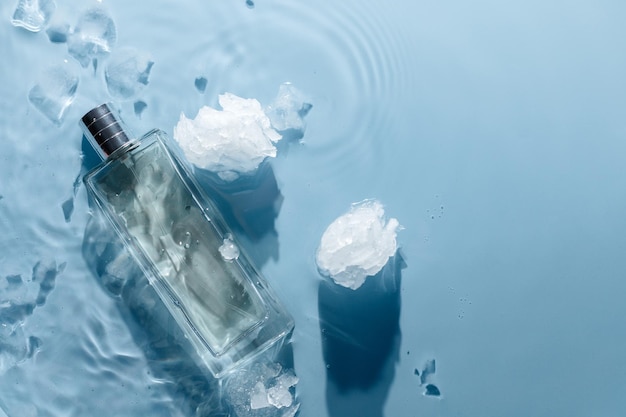 Frasco de perfume sobre fondo ondulado de agua azul con trozos de hielo Concepto de fragancia de agua fría fresca
