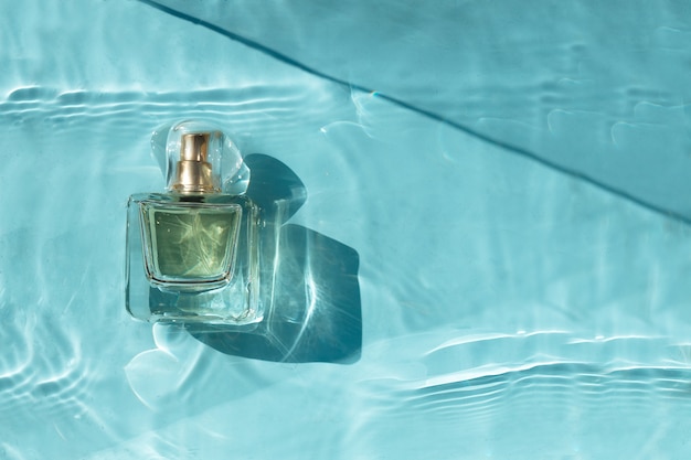 Frasco de perfume transparente en agua azul con sombras.