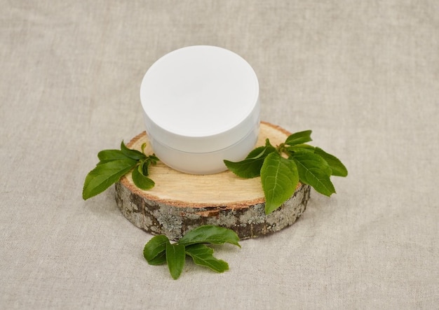 Un frasco de plástico blanco para cosméticos se encuentra en un podio de madera con hojas jóvenes verdes sobre un fondo de tela de lino color pastel Fondo cosmético ecológico