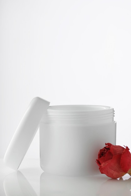 Frasco de plástico blanco vacío con tapa abierta sobre fondo claro Pétalos de rosas rojas Cosméticos rejuvenecedores